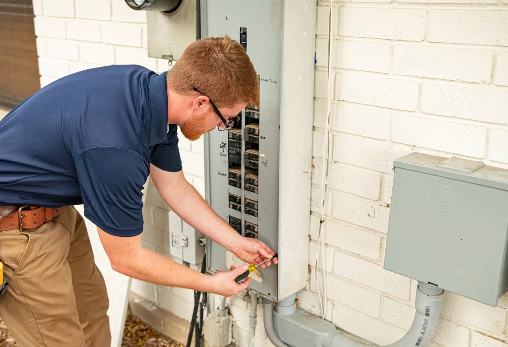 Electrician inspecting and testing a residential electrical panel with a multimeter.
