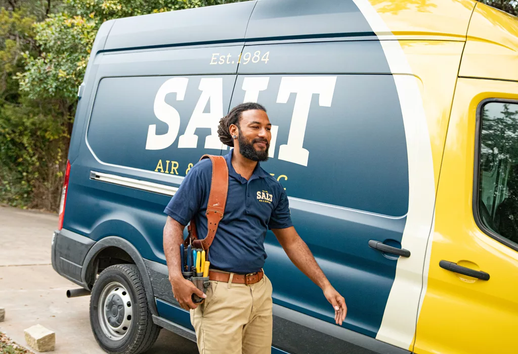 SALT technician in navy uniform carrying a tool belt, walking beside a branded company service van