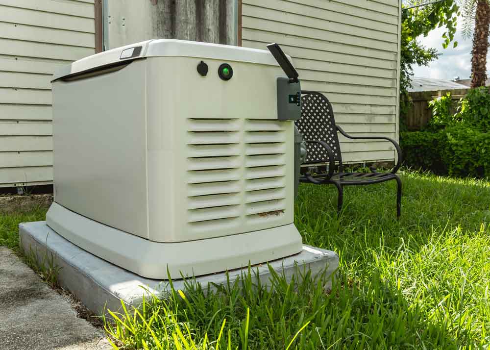 Standby whole-house generator installed on a concrete pad in a grassy backyard next to a home, ready for emergency power supply