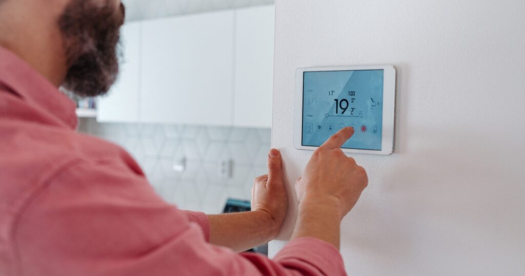 A man adjusting a digital smart thermostat on a wall to control indoor temperature