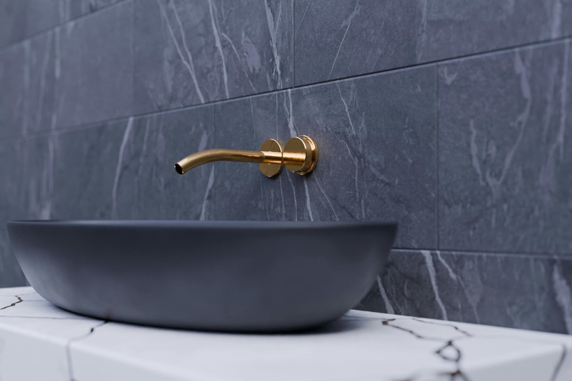 Gold wall-mounted luxury faucet over a modern basin, highlighting faucet finish aesthetics and durability.