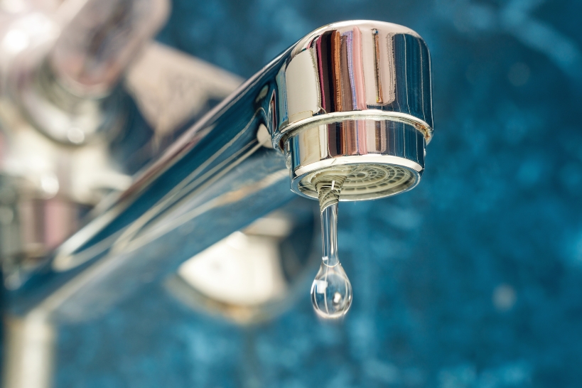 Close-up of a dripping faucet showing a common household leak that may need repair.