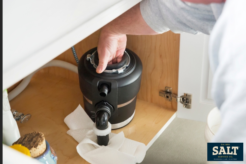 Person removing a garbage disposal under a kitchen sink during repair or replacement work.