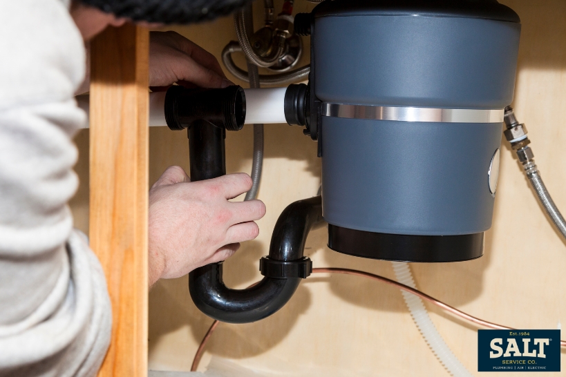 Person checking sink plumbing and a garbage disposal under the cabinet before resetting the unit.