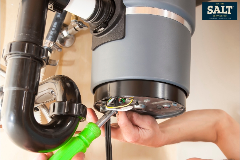 Close-up of a person working under a sink to unjam a garbage disposal using a hex wrench.